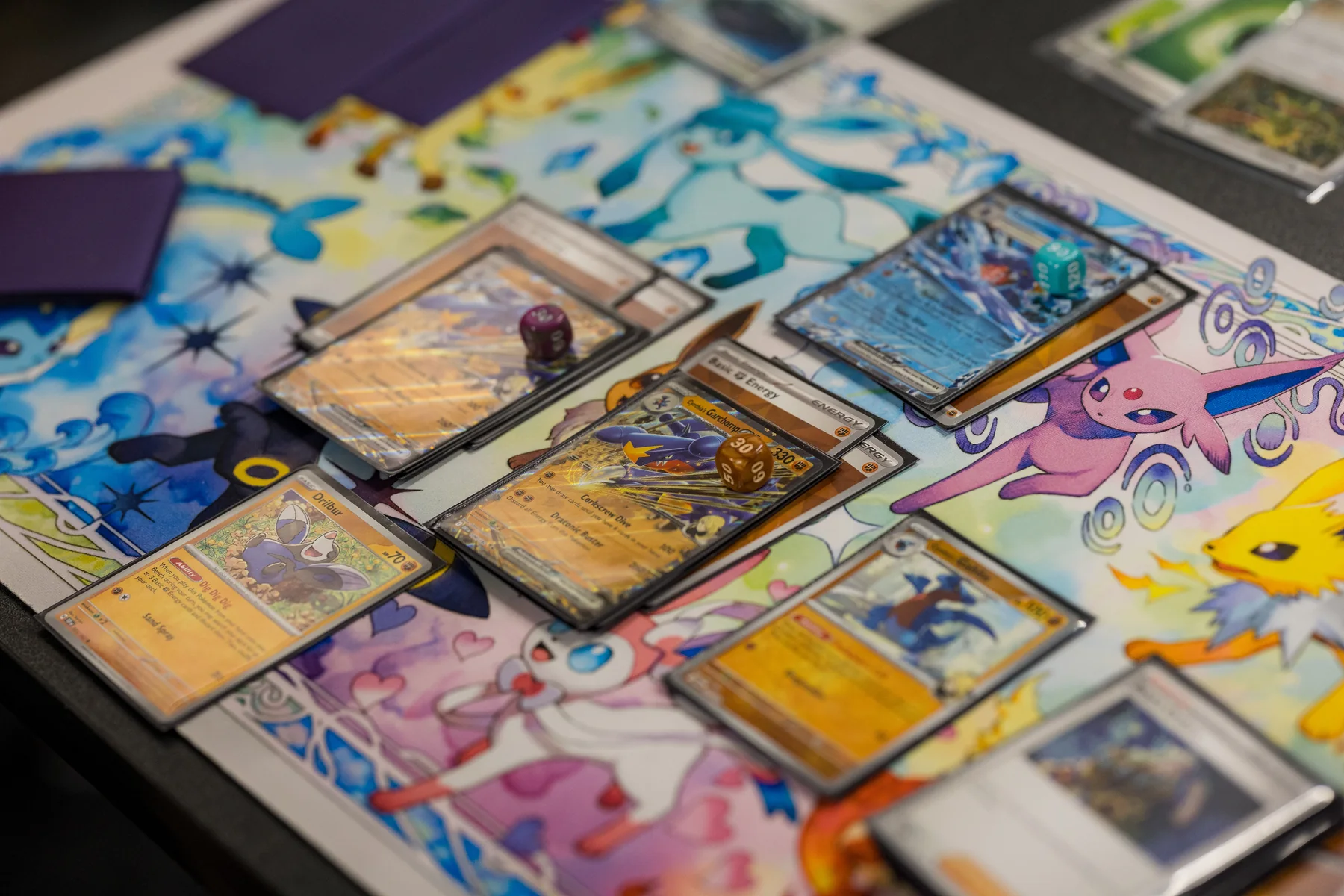 Trading cards, sleeves, and dice on a playmat at Izzi's Gym